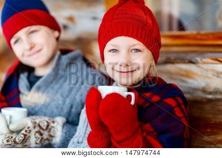Kids outdoors on beautiful winter day drinking hot chocolate in front of log cabin vacation house