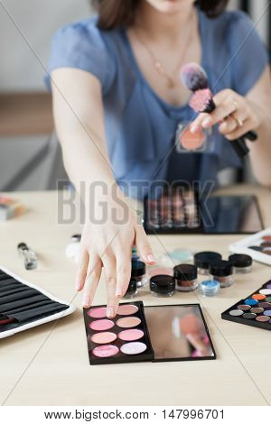 Artist taking rouge with brush, visagiste workplace. Close-up of stylist hand on palette with pink shades bluster. Beauty, makeup, cosmetics concept