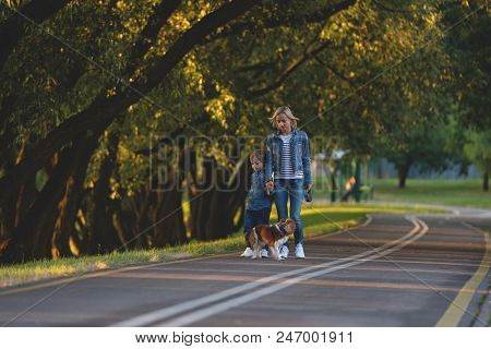 Concept Of Happy Young Mother With Adorable Kids And Dog Walking In Park