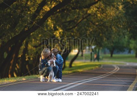 Concept Of Happy Young Mother With Adorable Kids And Dog Walking In Park