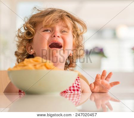 Beautiful blond child eating spaghetti with hands crying with tantrum at home.