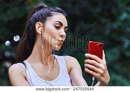 Young Girl Is Taking Picture Of Herself Using Red Cell Phone And Listening To The Music Using White 