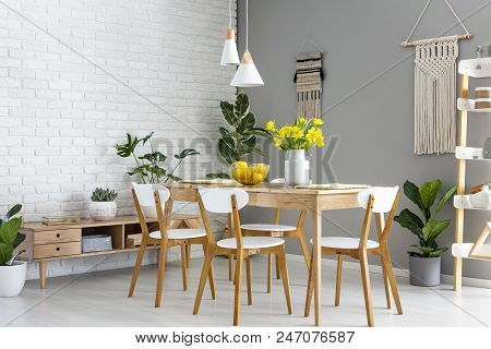 White Lamps Above Wooden Table And Chairs In Dining Room Interior With Yellow Flowers. Real Photo