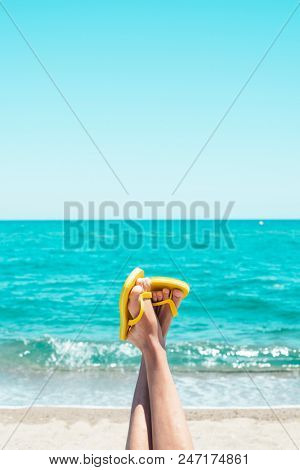closeup of the legs of a young caucasian man on the beach, upside down, wearing a pair of yellow flip-flops, against the sky with a blank space on top