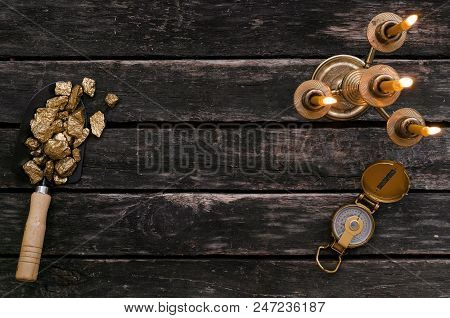 Gold Ore Nuggets In Shovel, Compass And Burning Candle On Old Adventurer Table. Goldminer Treasure H