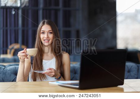 A Beautiful Girl Is Trinking A Cup Of Cappuccino On Her Working Place In The Office.