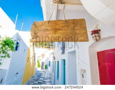 Wooden sign hanging on the rope under the roof. Signboard in front of narrow Greek street. Paros island, Greece