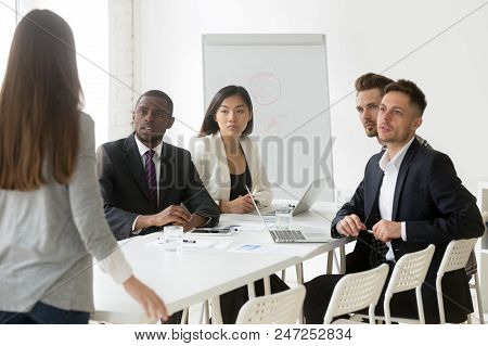 Diverse Millennial Team Looking Judgmental At Female Worker Being Late To Meeting, Angry Colleague S