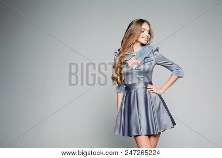 Attractive And Fashionable Blondie Girl In Dtylish Gray Dress Posing In Studio. Sedactive Woman Hold