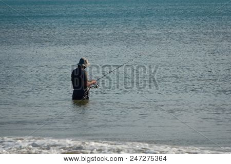 The Fisherman Catches Fish In The Sea On A Fishing Pole Standing In Water.