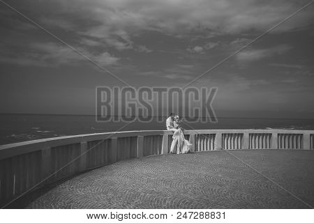 Beautiful Wedding Couple Of Blonde Standing Woman In Long Gauzy Dress And Man In White Sitting On St