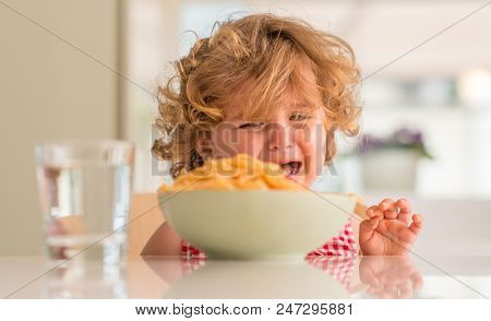 Beautiful blond child eating spaghetti with hands crying with tantrum at home.