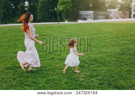 Laughing Woman In Light Dress Running Catching Up With Little Cute Child Baby Girl On Green Grass La