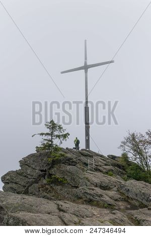 Woman In The Fog Stands Next To The Huge Summit Cross On The Kreutfelsen