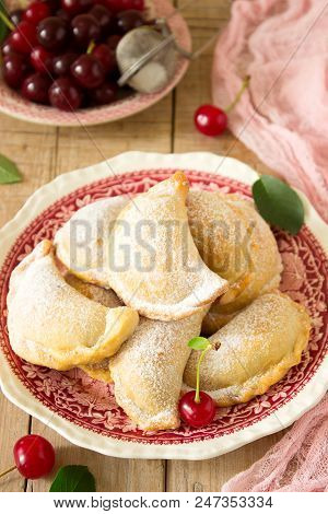 Pies With Cherries, Sprinkled With Powdered Sugar And Berries Of Fresh Cherries On A Wooden Surface.