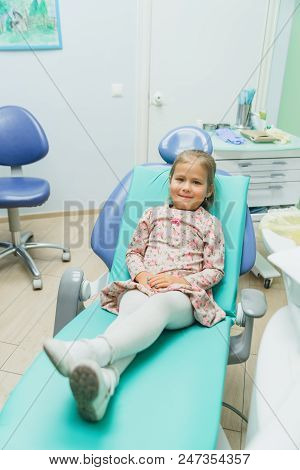 Child With A Mother At A Dentist's Reception. The Girl Lies In The Chair, Behind Her Mother. The Doc