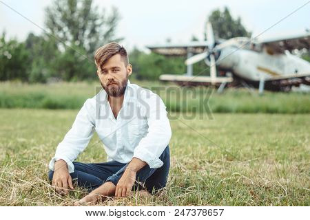 A Man In A Shirt Sitting On The Grass At The Old Plane