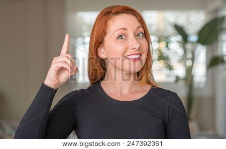 Redhead woman at home surprised with an idea or question pointing finger with happy face, number one