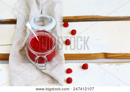 Raspberry Jam In A Glass Jar With A Spoon And Fresh Raspberry On White Wooden Background. Top View.