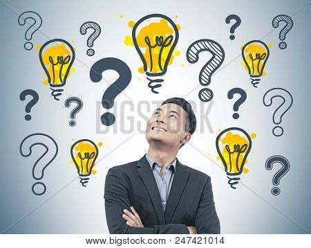 Confident And Cheerful Asian Start Up Founder In Suit Standing Near A Gray Wall With Many Question M
