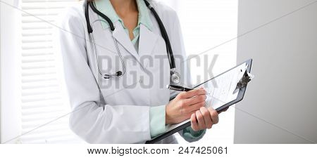 Female Doctor Filling Up Medical Form On Clipboard Closeup.  Healthcare, Insurance And Medicine Conc
