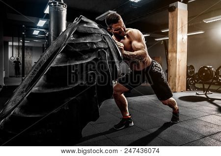Muscular Bearded Tattooed Fitness Shirtless Man Moving Large Tire In Gym. Concept Lifting, Workout C