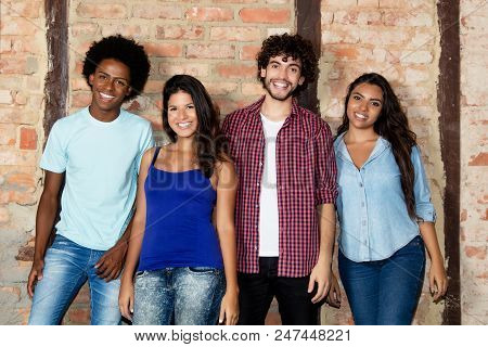 Group Of Happy Multiethnic Young Men And Women Indoor Looking At Camera In Front Of Brickstone Wall