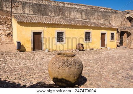 Yellow Wall Of An Old House, Part Of Castro Marim Castle. Windows With Stone Frames And A Grating. T