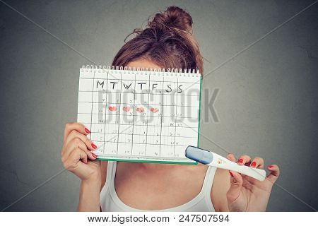 Young Woman Hiding Behind A Periods Calendar And Showing A Positive Pregnancy Test