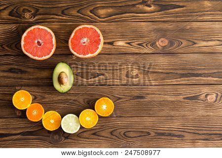 Fresh Halved Fruit Arranged In Smiling Face On Wooden Background With Copy Space.