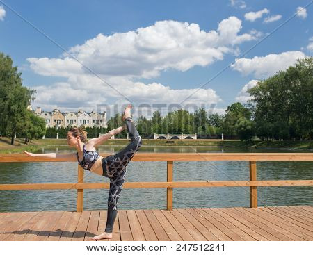 Young Slim Girl In Grey Sport Wear Doing Yoga On The Bridge. Flexible Young Girl With Red Hair.