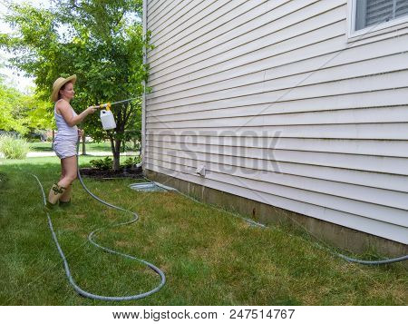 Attractive Housewife Spraying Down The Exterior Facade Of Her Home Washing The Timber Sidings With A
