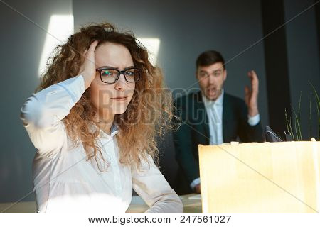 Upset Stressed Young Female Worker In Glasses Holding Head, Looking At Camera, Sitting At Desk With 