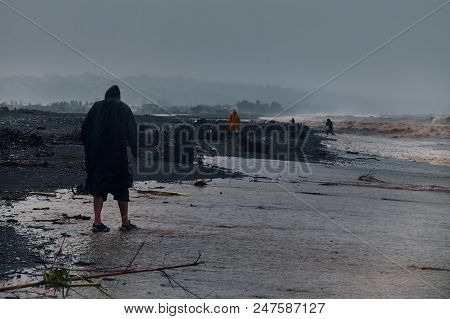 Man In A Raincoat Walking At The Stormy Sea With Huge Dirty Waves