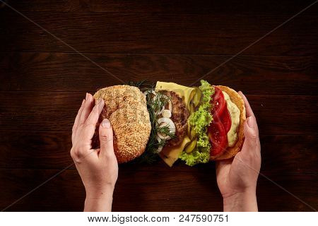 Woman's Hands Holding Traditional American Burger On Wooden Background, Top View, Close-up.