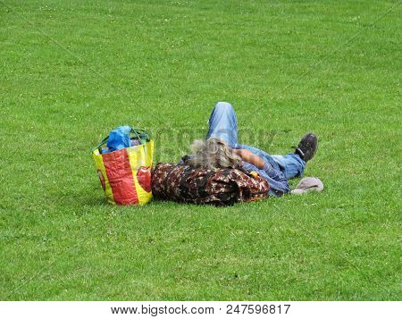 An Older Caucasian Male Man With Long Grey Hair Lying And Sleeping On Green Grass