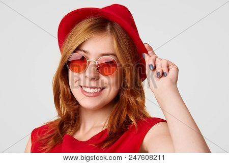 Beautiful Stylish Female Stands Sideways, Touches Fashionable Red Hat, Wears Trendy Sunglasses, Like