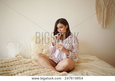 Cute Chubby Girl In Striped Nightsuit, Sitting Cross Legged On Bed In Her Room, Holding Glass Of Fre