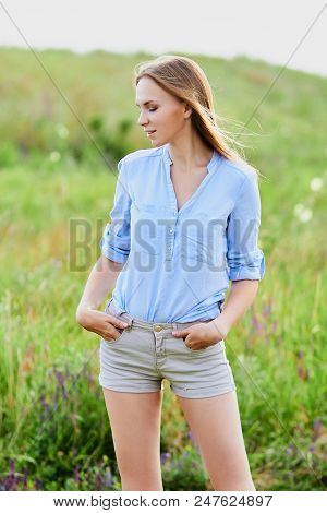 Happy Smiling Young Girl In Blue Shirt And Shorts In The Field