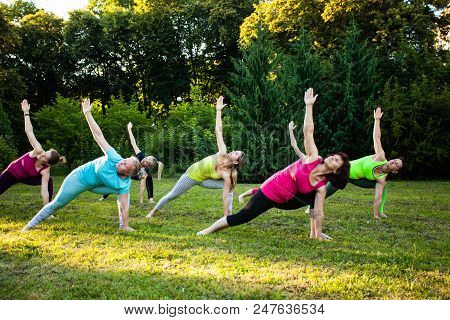 Group Of Adult Women Attending A Yoga Class Outdoors, Triangle Pose