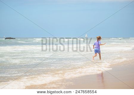 Happy Girl In Purple Swimsuit Running On The Beach In The Waves, Family On Vacation, View From Behin