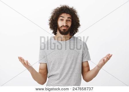 Indoor Shot Of Clueless Confused Hispanic Boyfriend With Afro Hairstyle And Masculine Beard, Raising