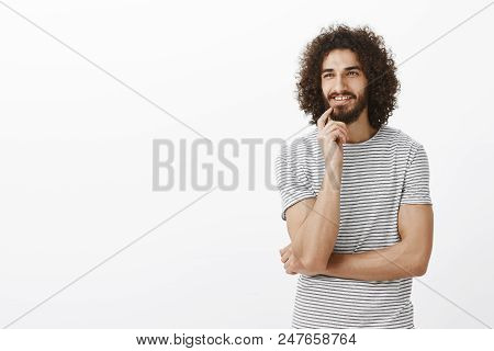 Intrigued Happy Bearded Male With Afro Hairstyle And Beard, Looking Aside, Holding Finger On Lip And