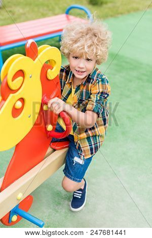 High Angle View Of Happy Curly Boy Riding On Rocking Horse At Playground