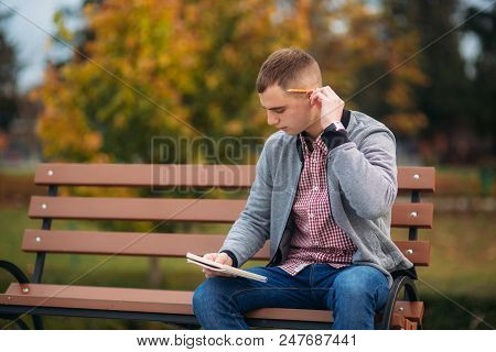 A Cute Student Writes Down His Thoughts In His Notebool Using A Pensil.