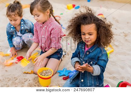 Selective Focus Of Curly African American Child Playing Wit Friends In Sandbox At Playground