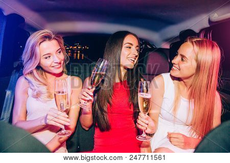Positie And Gorgeous Girlsare Sitting In Car And Having Fun. They Are Holding Glasses With Champagne