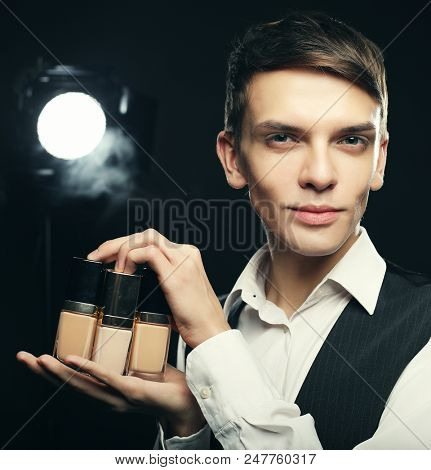 Beauty concept. Young male make up artist posing with foundation for make-up on a dark background.