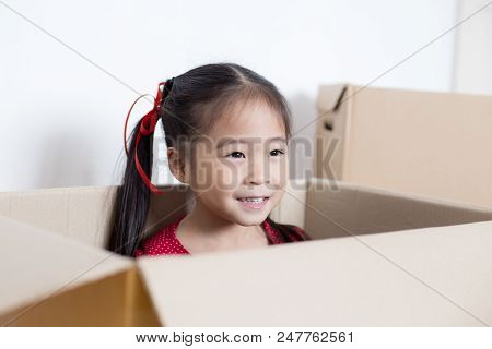 Asian Girl Playing In The Box At Home. Kid Sitting Inside Box With Attractive Smiling.