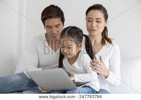 Attractive Little Girl Using Laptop With Mom And Dad Together. Girl Learning To Use Laptop. Happy Fa